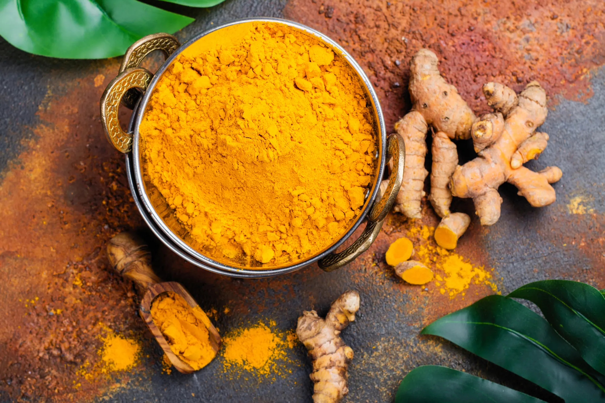 Curcuma en poudre dans un bol en laiton et racines de curcuma frais sur une table