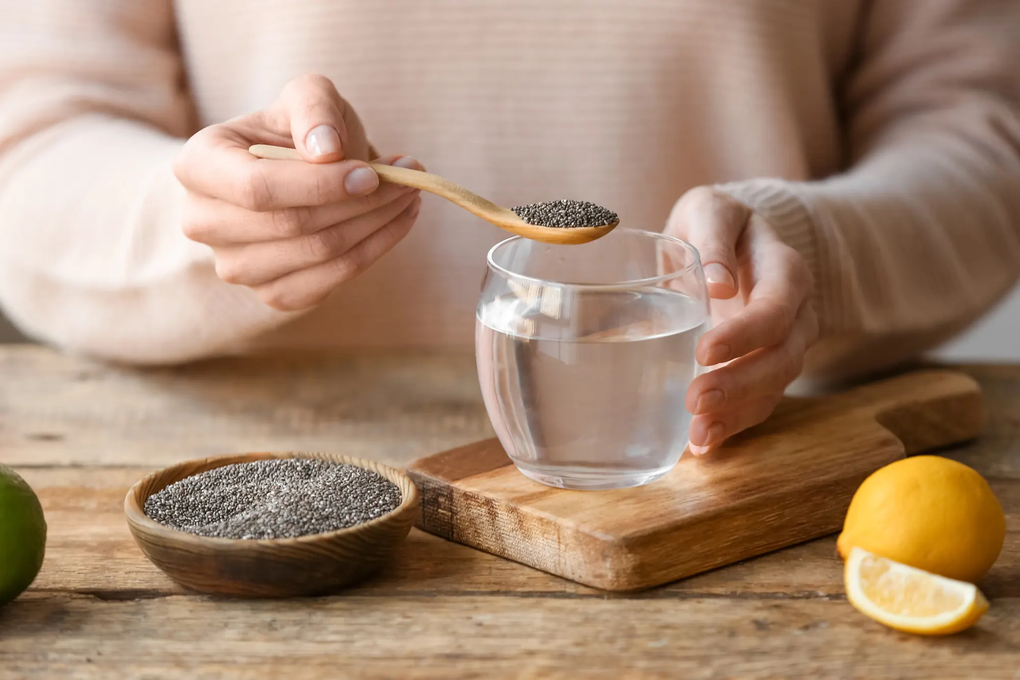 Une femme verse une cuillère de graines de chia dans un verre d’eau