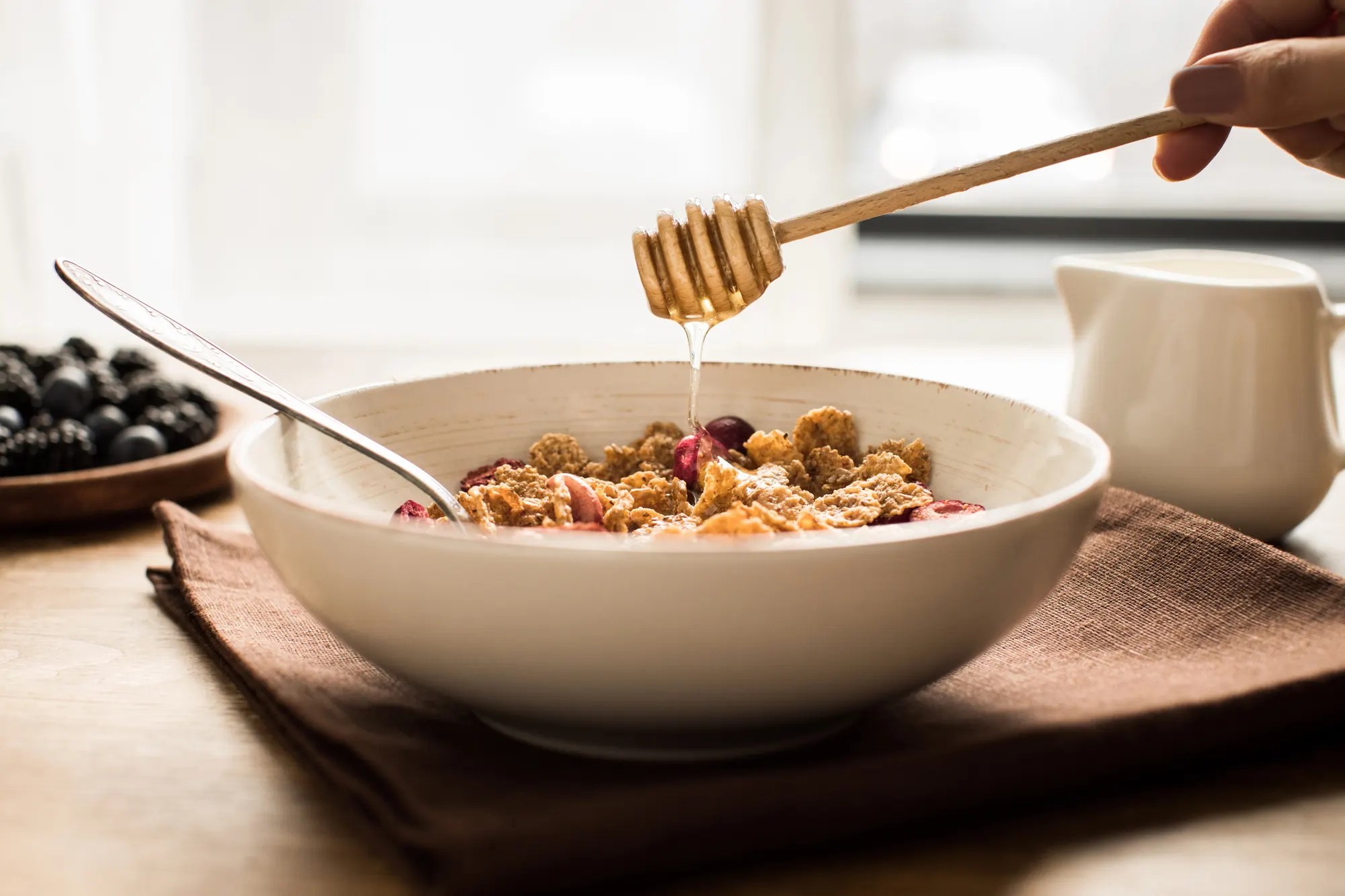 Du miel coule d’une cuillère en bois sur un bol de céréales du petit-déjeuner