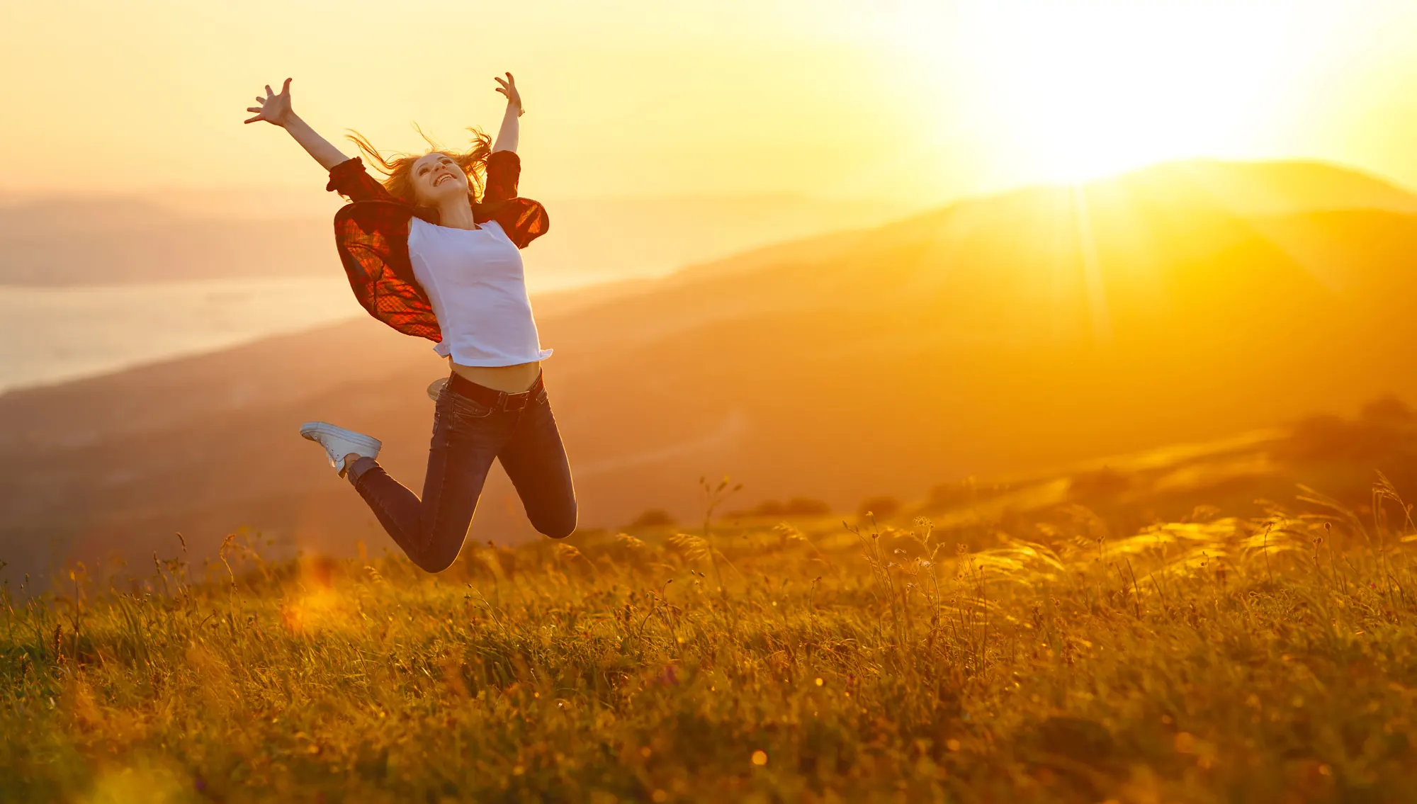 Une femme saute de joie dans un champ au soleil couchant